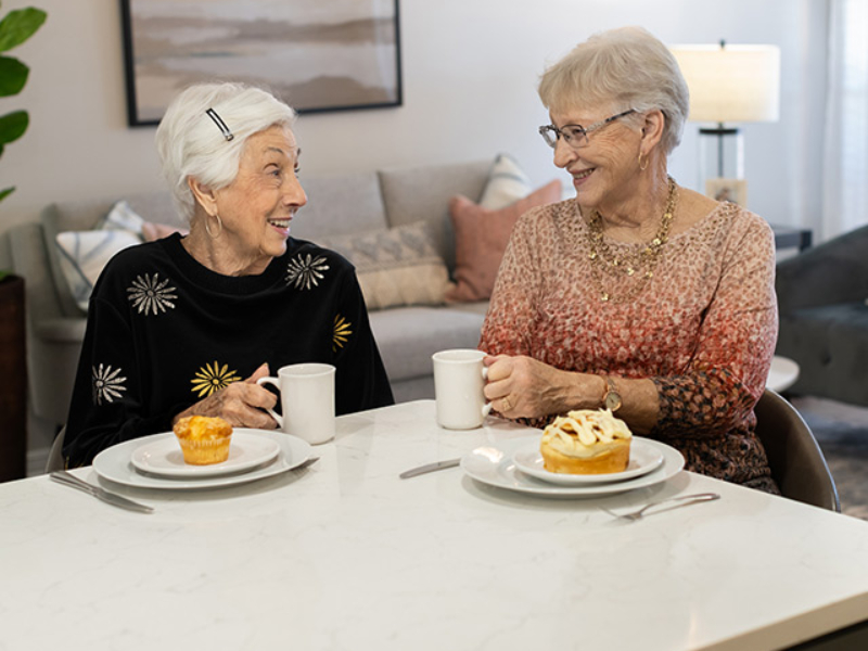 AL-640x600 Two senior women enjoying breakfast pastries over coffee.