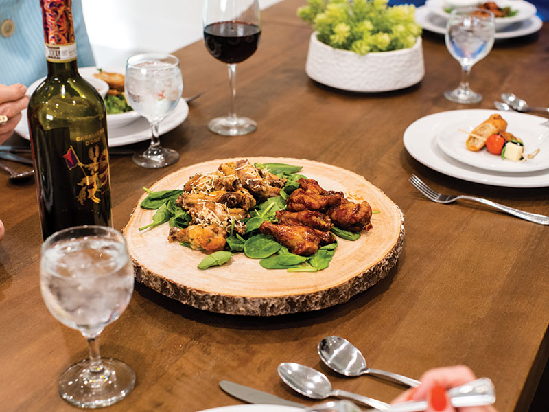 Chicken wings on wooden platter on a dining table with wine and glasses