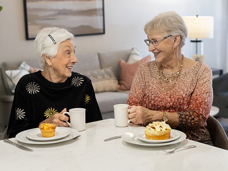 Two senior women enjoying a mug of coffee and breakfast pastries