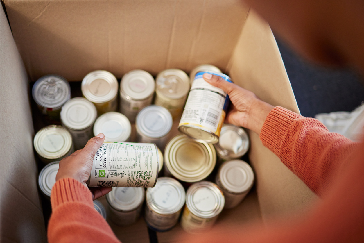 Donation, food in cans in box and hands of man checking stock, decision and volunteer with ngo help. Support with charity, choice and refugee at grocery distribution for sustainable community service canned food drive