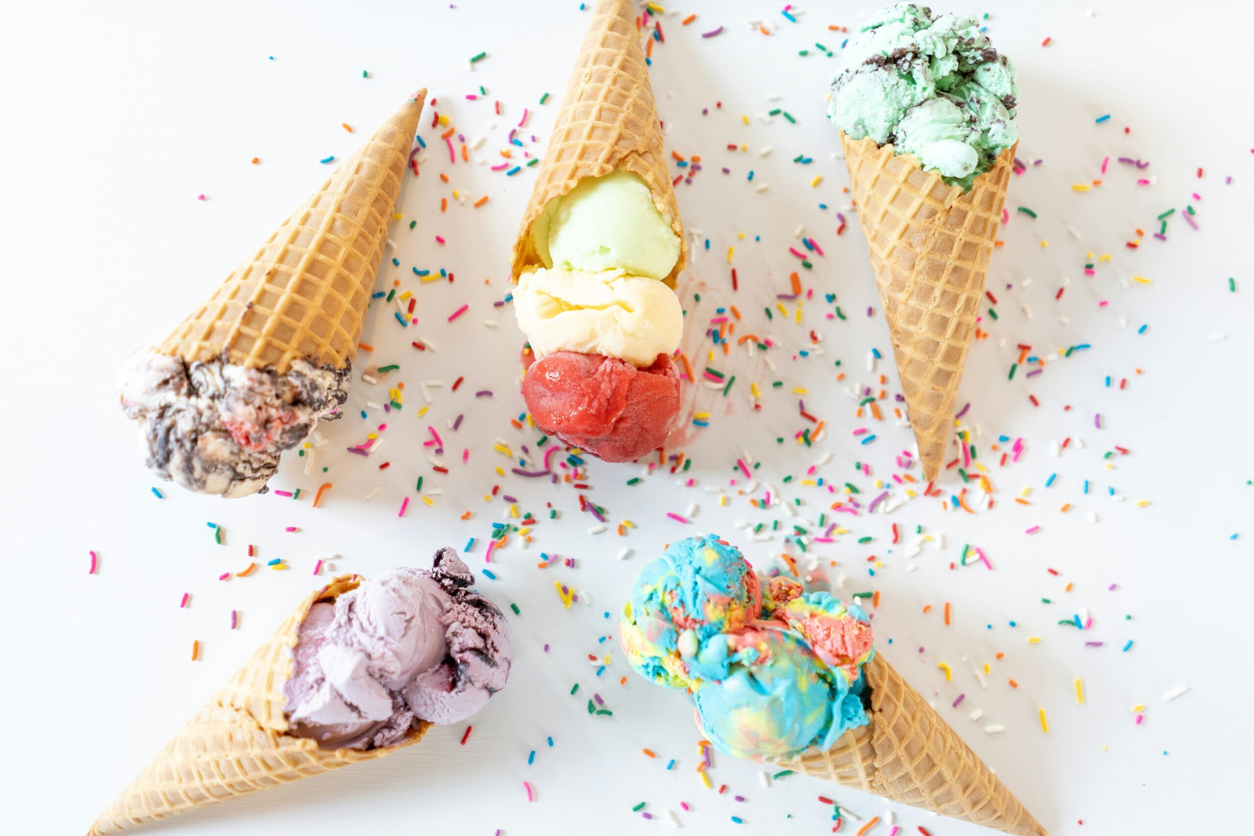 5 ice cream cones with various flavors laid down on a white table