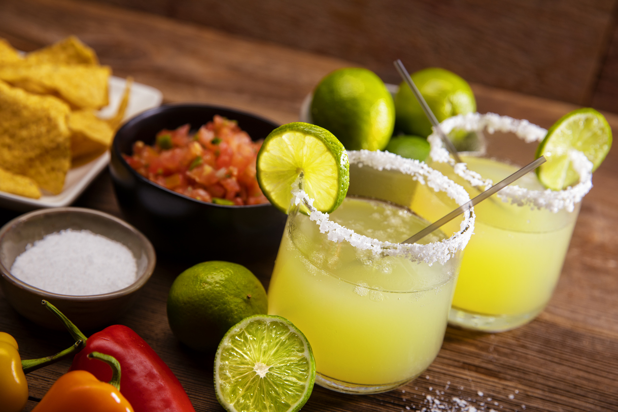 Margarita glasses on a retro Wood Background This is a photograph of two modern margarita glasses with a rim of salt surrounded by fresh cut limes and chips and salsa on a retro wood background