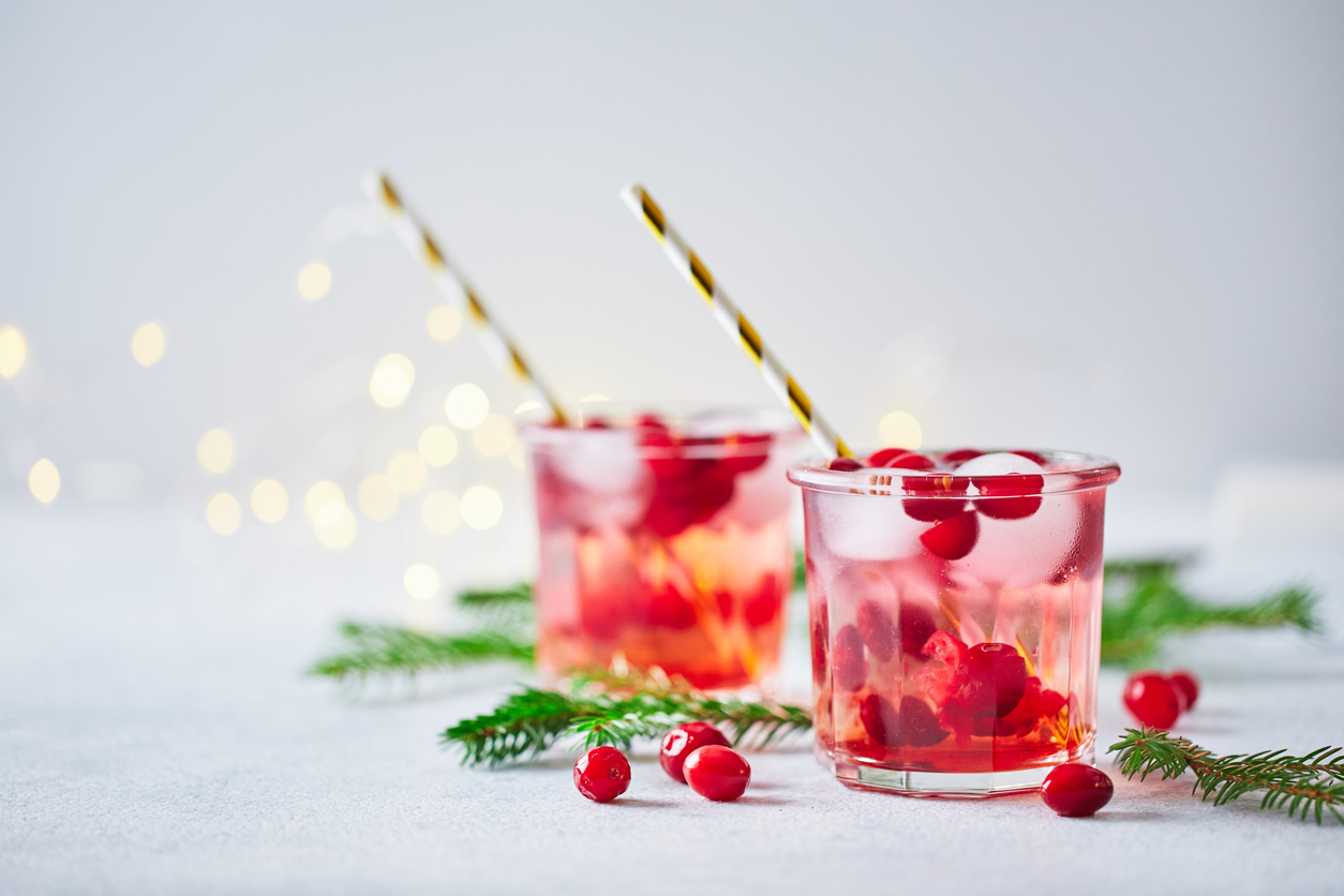 Alcoholic cocktail or non-alcoholic mocktail with vodka and iced cranberries with fir branches and glowing garland for christmas.