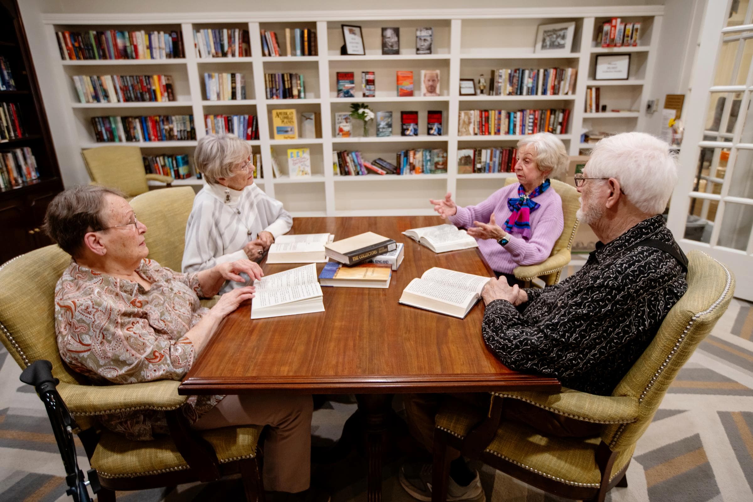 Senior friends are involved in a discussion around a table in the library