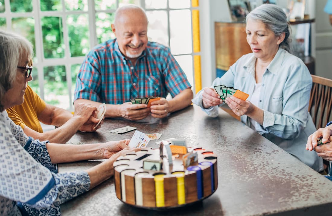 senior friends playing cards around a table indoors