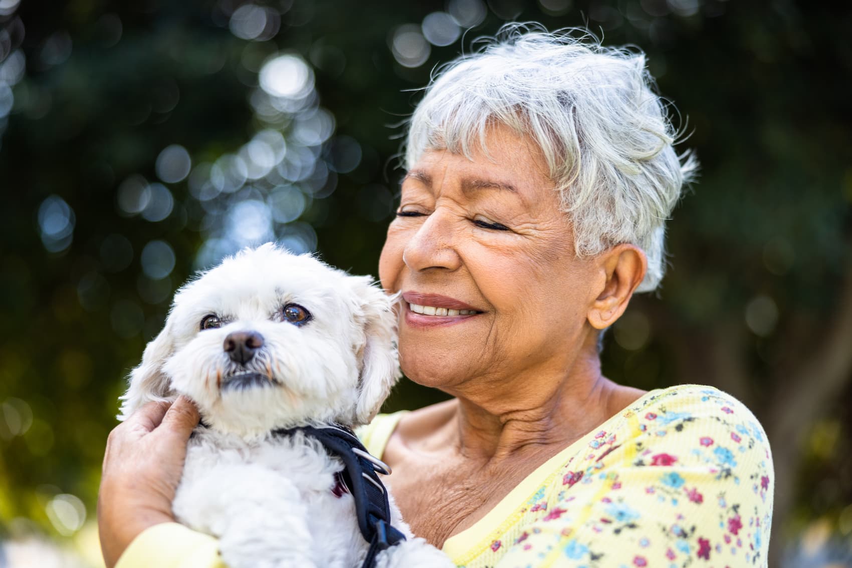senior woman holding white dog and smiling outdoors