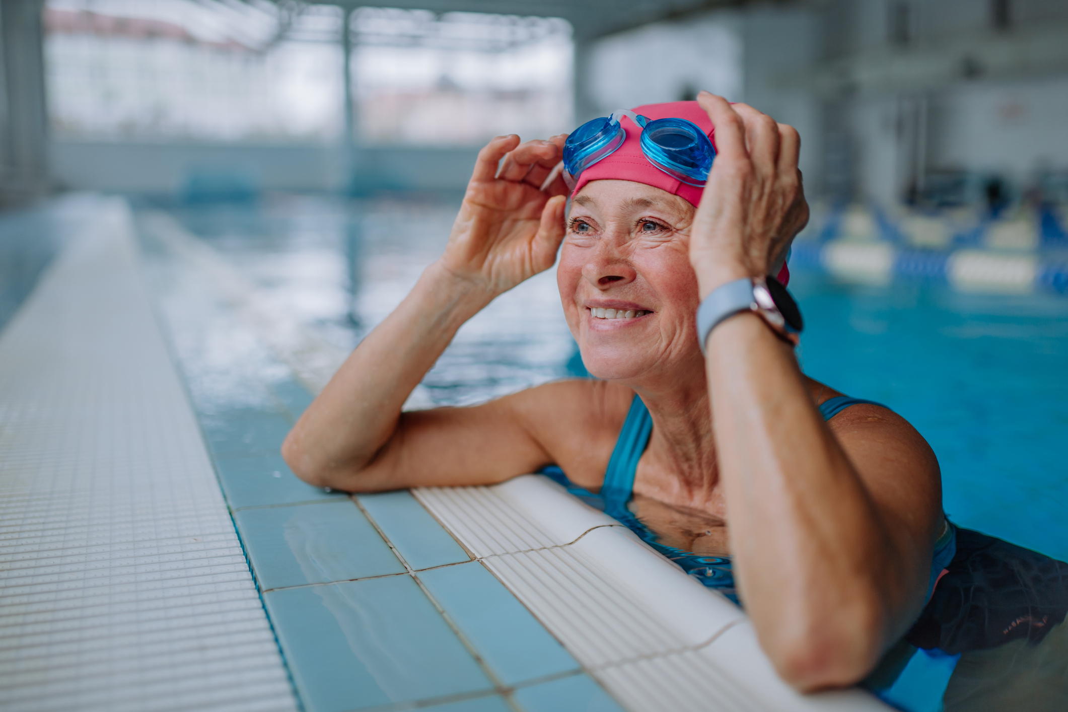 senior woman on the side of an indoor pool smiling
