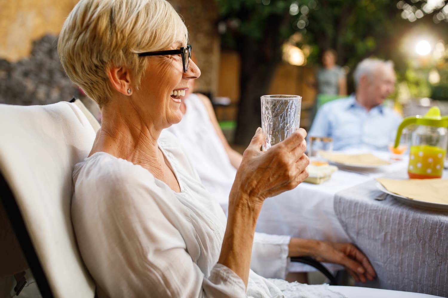 Smiling older woman enjoying a drink outdoors at a social gathering.
