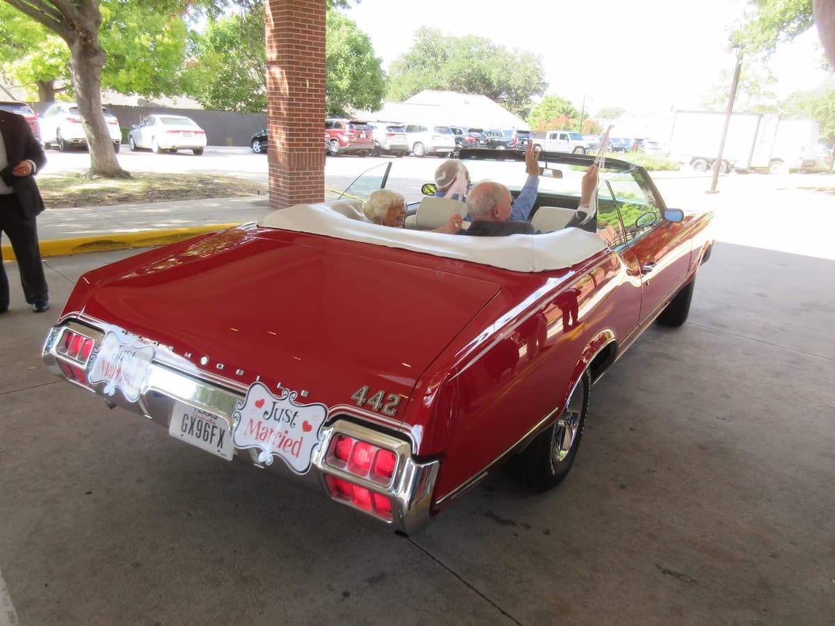 Bill and Sharon Hampton driving away in vintage red call that says 'Just Married'